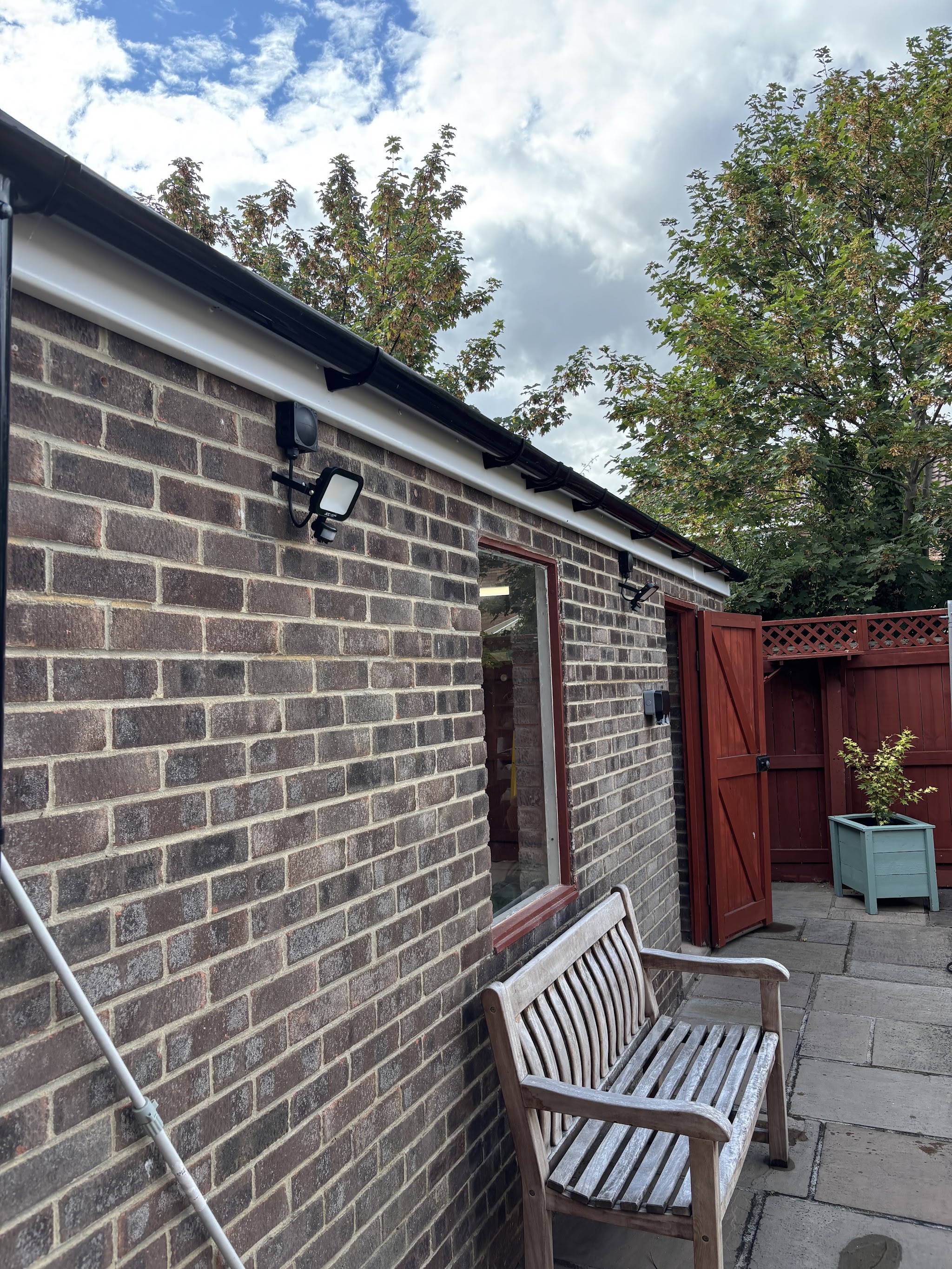 Outdoor security floodlight fitted to a brick garden building